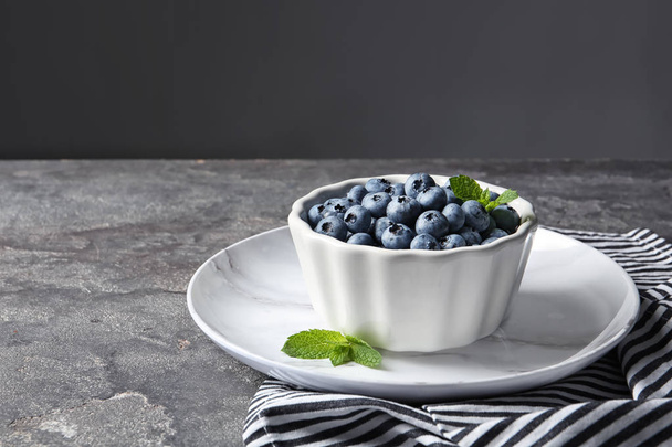 Crockery with juicy blueberries on color table - Fotó, kép