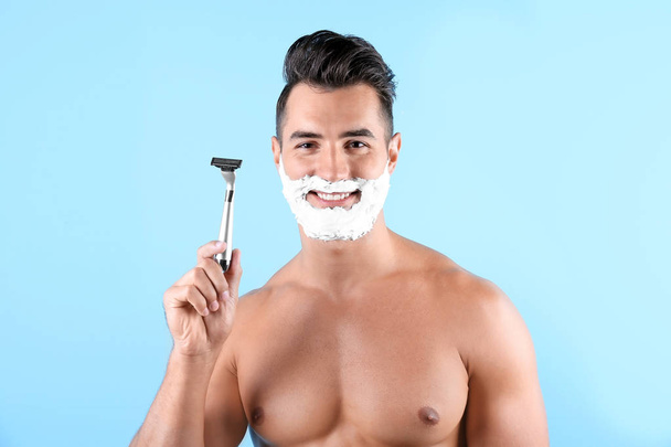 Handsome young man with shaving foam and razor on color background - Foto, Imagen