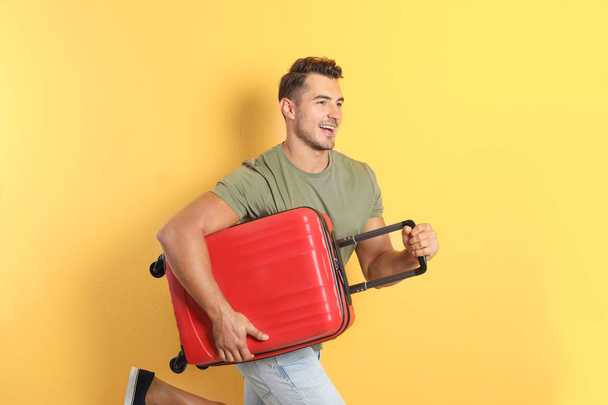 Young man running with suitcase on color background - Foto, afbeelding