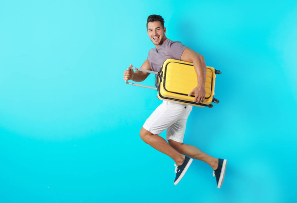 Young man jumping with suitcase on color background. Space for text - Фото, зображення