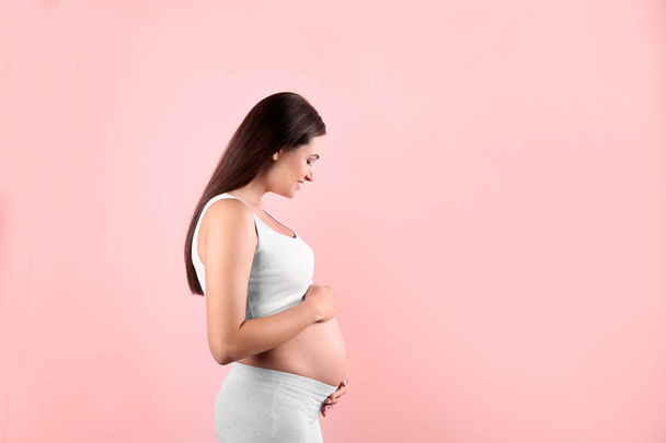 Beautiful pregnant woman holding hands on belly against color background. Space for text - Photo, image