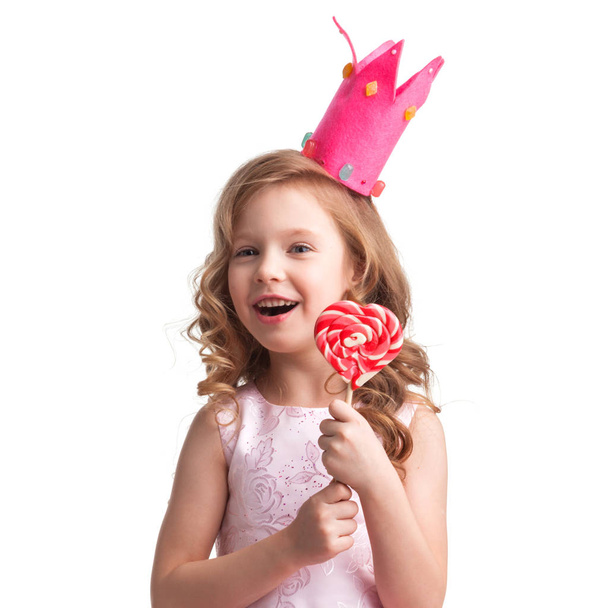 Krásná malá holčička candy princezna v koruně drží velké růžové srdce tvarovaný lízátko a usmívá se - Fotografie, Obrázek