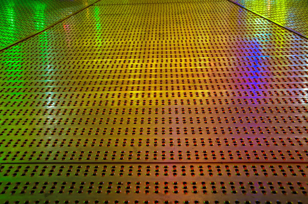 Reflejo de luces de colores sobre un suelo de hierro con perforaciones
  - Foto, imagen