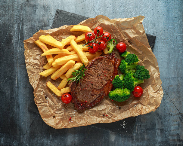 Grilled sirloin steak with potato fries, broccoli and cherry tomatoes on crumpled paper - Photo, Image
