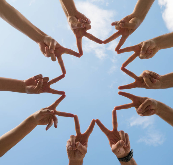 un cercle de dix mains faisant des signes de paix sous un ciel bleu avec des nuages blancs
 - Photo, image