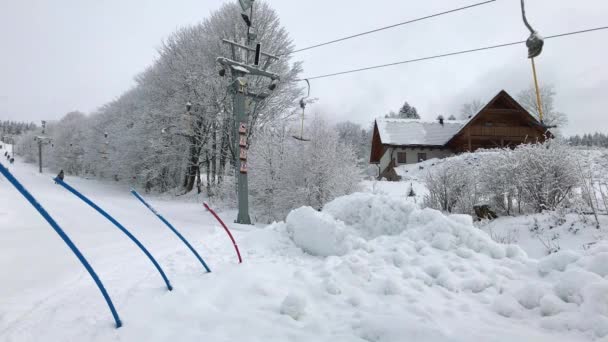Twee schoten van skilift op besneeuwde skiresort, ouder met kind, skiërs op ski's lift omhoog op stoeltjeslift op bewolkte dag van de winter, Sneeuwwitje afhankelijke bomen op de randen, huis dak in de buurt van ski heuvel - Video
