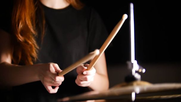 Rudowłosa dziewczyna gra muzyka drums w ciemnym studio. Ręce, pałeczka do bębenka. - Zdjęcie, obraz