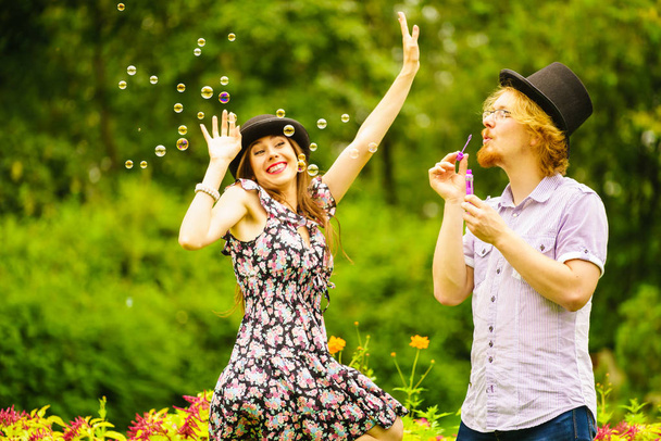 Happy funny hipster couple playing together blowing soap bubbles outdoor in spring park. - Photo, Image