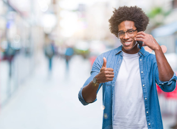 Афро-американец говорит по телефону на изолированном фоне счастливый с большой улыбкой делает хорошо знак, палец вверх пальцами, отличный знак
 - Фото, изображение