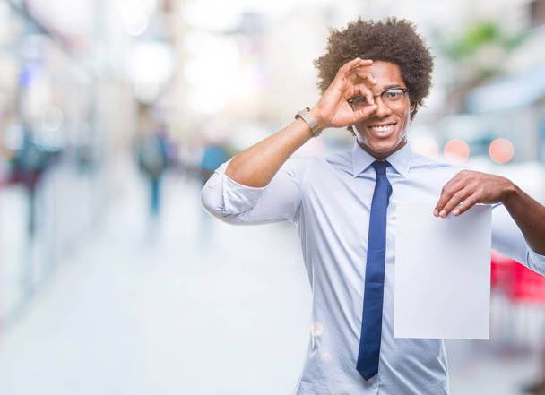 Αφρο αμερικανικό άνθρωπος που κρατά κενό χαρτί σύμβαση πέρα από το απομονωμένο υπόβαθρο με χαρούμενο πρόσωπο χαμογελά κάνει εντάξει σημάδι με το χέρι στο μάτι που αναζητούν μέσα από τα δάχτυλα - Φωτογραφία, εικόνα