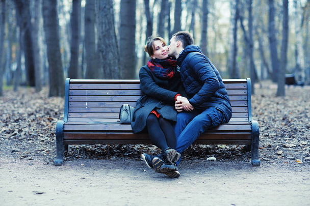 young man and woman sitting on bench together in winter park, romantic happy couple - Foto, afbeelding