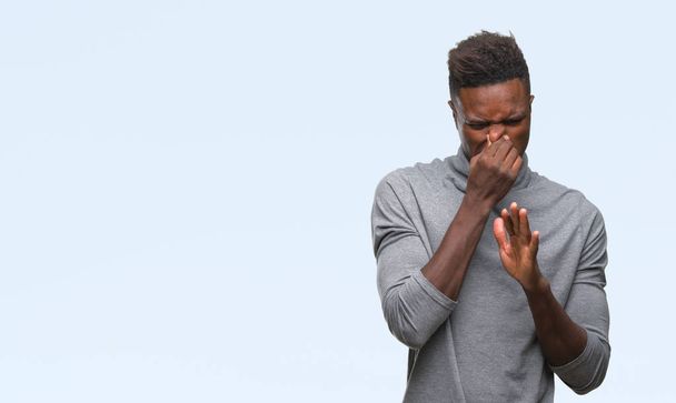 Young african american man over isolated background smelling something stinky and disgusting, intolerable smell, holding breath with fingers on nose. Bad smells concept. - Photo, Image
