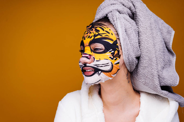 a funny young girl with a towel on her head wants to be beautiful, on her face a moisturizing mask with leopard mordants - Fotó, kép