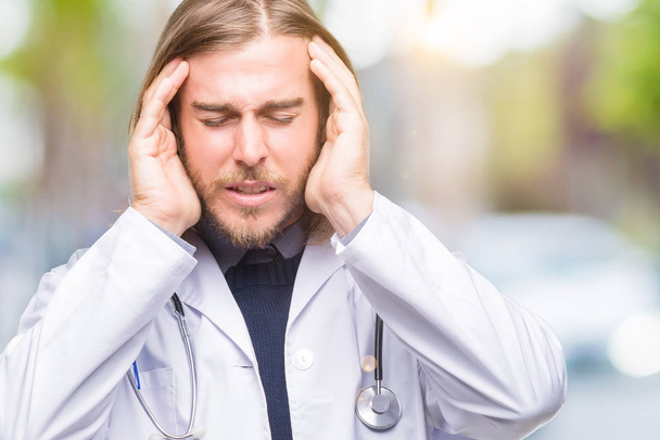 Young handsome doctor man with long hair over isolated background with hand on head for pain in head because stress. Suffering migraine. - Photo, Image