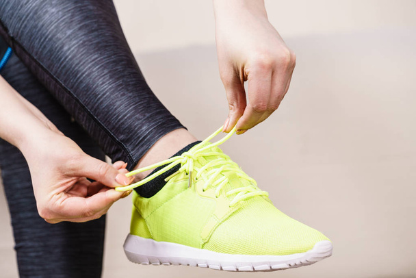 Woman in sportswear sitting on sofa indoor getting ready for exercises. Tying up shoes - 写真・画像