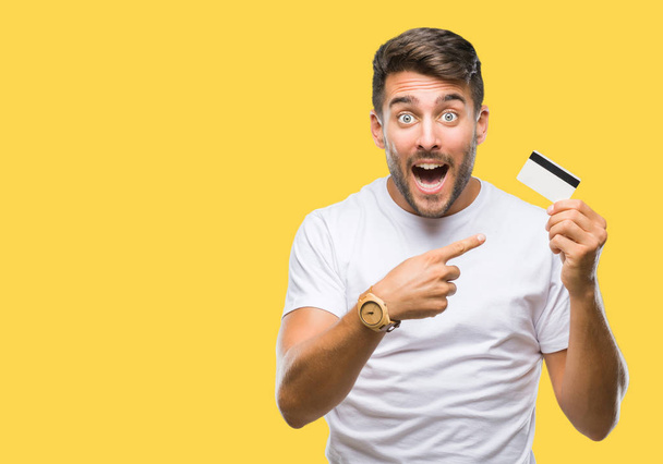 Молодий красивий чоловік тримає кредитну картку над ізольованим тлом дуже щасливий, вказуючи рукою і пальцем
 - Фото, зображення