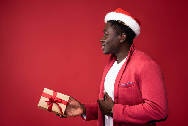 Joyful guy is holding gift on red background - Zdjęcie, obraz