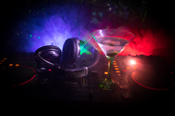 Glass with martini with olive inside on dj controller in night club. Dj Console with club drink at music party in nightclub with disco lights. - Photo, Image