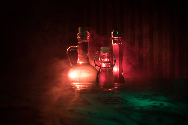 Frascos de vidrio antiguos y vintage sobre fondo oscuro brumoso con luz. Concepto de veneno o líquido mágico
. - Foto, Imagen