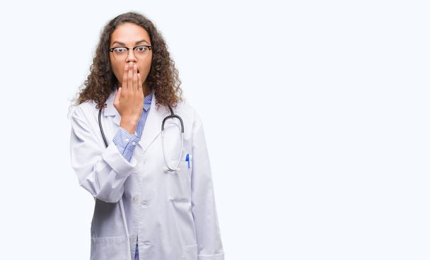 Νέος Ισπανικός γιατρός γυναίκα κάλυψη στόμα με το χέρι σοκαρισμένος με ντροπή για λάθος, έκφραση του φόβου, φοβάται στη σιωπή, μυστική έννοια - Φωτογραφία, εικόνα