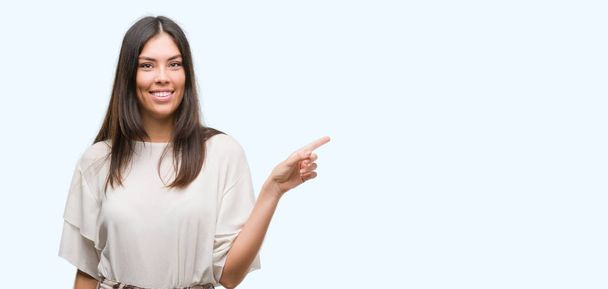 Young beautiful hispanic woman very happy pointing with hand and finger to the side - Photo, Image