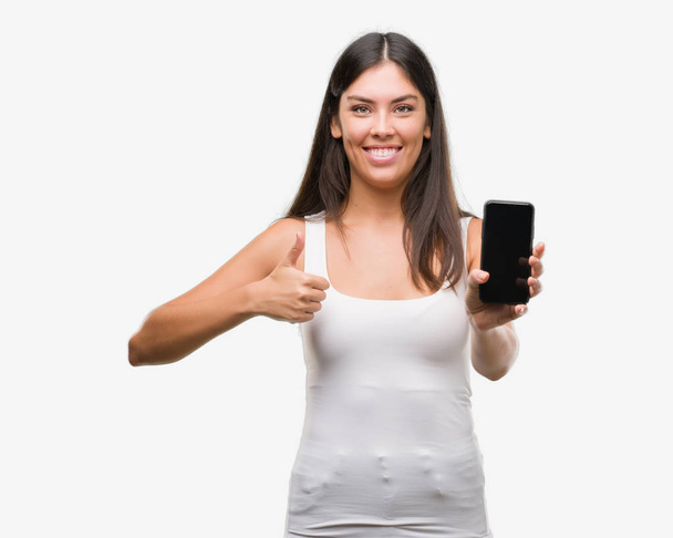 Young beautiful hispanic showing smartphone happy with big smile doing ok sign, thumb up with fingers, excellent sign - Foto, Bild