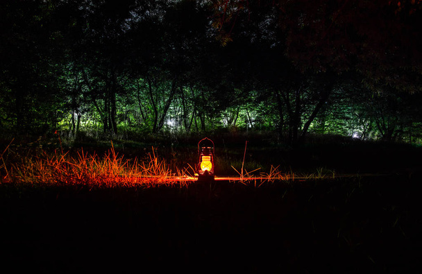 Horror Halloween concept. Burning old oil lamp in forest at night. Night scenery of a nightmare scene. Selective focus. - Photo, Image