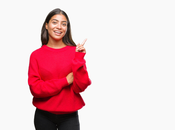 Young beautiful arab woman wearing winter sweater over isolated background with a big smile on face, pointing with hand and finger to the side looking at the camera. - Zdjęcie, obraz