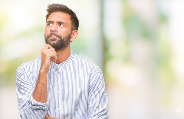 Adult hispanic man over isolated background with hand on chin thinking about question, pensive expression. Smiling with thoughtful face. Doubt concept. - Foto, immagini