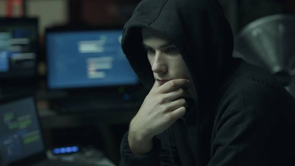 Young hacker with a hoodie thinking with hand on chin and working with computers, technology and cybercrime concept - Foto, Bild