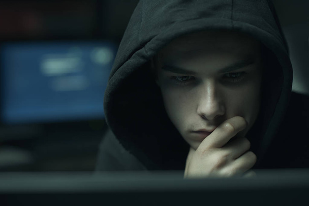 Cool young hacker with hoodie working with computers, cybercrime and data security concept - Фото, изображение