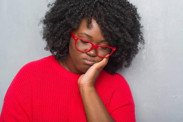 Giovane afro-americana plus size donna oltre grigio grunge parete indossando maglione invernale pensando cercando stanco e annoiato con problemi di depressione con le braccia incrociate
. - Foto, immagini