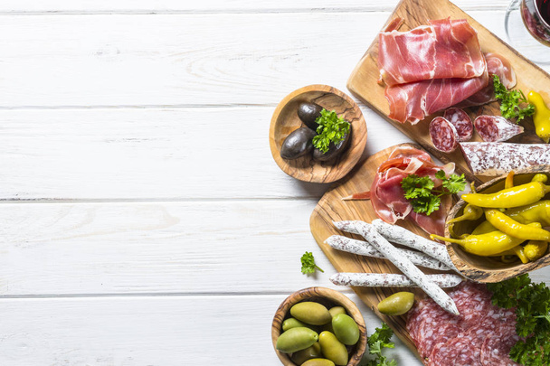 Antipasto italiano tradicional, carne cortada en rodajas con vino y aceitunas sobre mesa blanca. Vista superior, espacio de copia
. - Foto, imagen