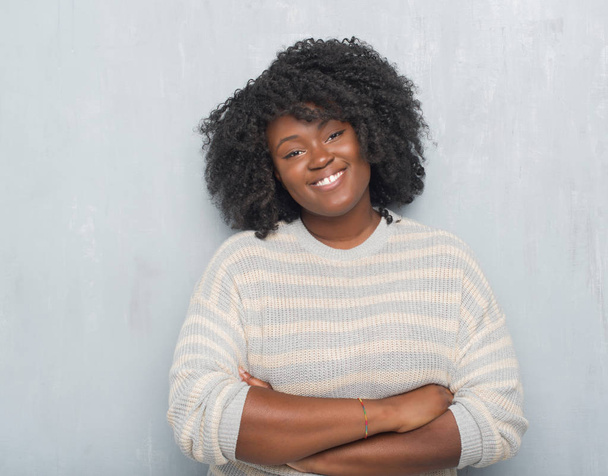 Giovane afroamericana plus size donna sopra il muro grigio grunge indossa un maglione volto felice sorridente con le braccia incrociate guardando la fotocamera. Persona positiva
. - Foto, immagini