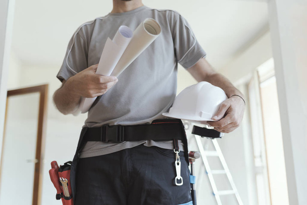 Professional construction engineer holding paper rolls and a safety helmet, home renovation and architecture concept - Photo, image