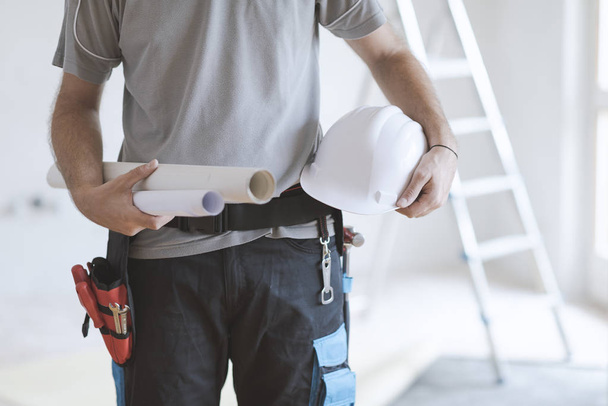 Professional construction engineer holding paper rolls and a safety helmet, home renovation and architecture concept - Foto, Imagen