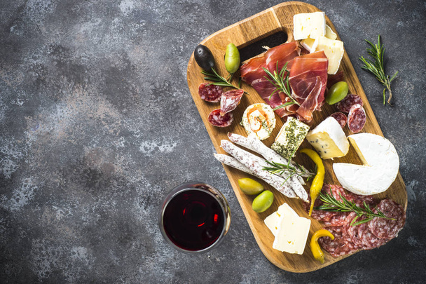 Antipasto board with sliced meat, ham, salami, cheese, olives and red wine. Top view with copy space. - Photo, Image