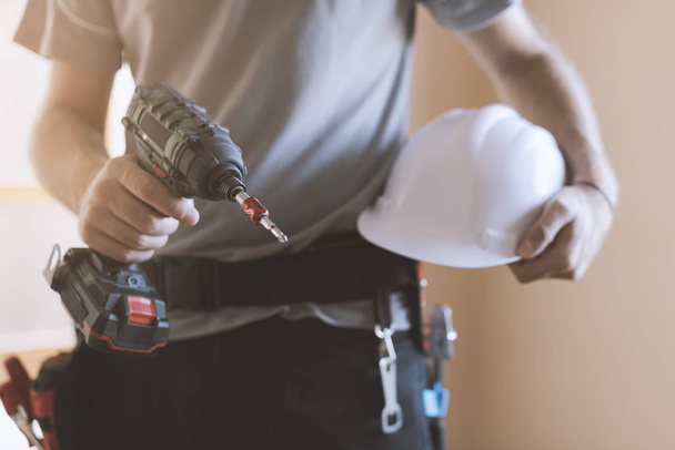 Construction worker posing with safety helmet and drill, home renovation and construction concept - Zdjęcie, obraz