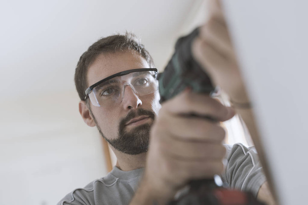 Professional repairman with protective goggles, he is using a drill and doing a home renovation - Foto, imagen