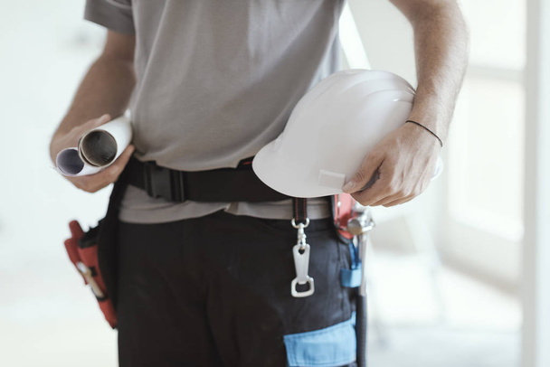 Professional construction engineer holding paper rolls and a safety helmet, home renovation and architecture concept - Photo, image