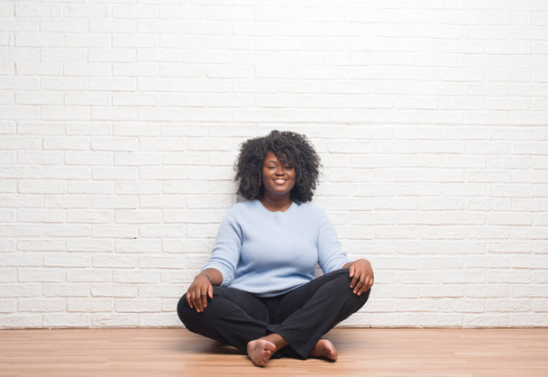 Giovane donna afroamericana seduta sul pavimento a casa con un sorriso felice e fresco sul viso. Persona fortunato
. - Foto, immagini