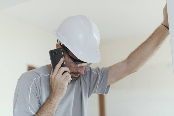 Professional builder with safety helmet having a phone call, home renovation and communication concept - Foto, Imagem