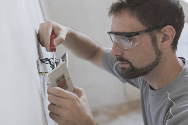 Professional electrician installing sockets using a screwdriver: home renovation and maintenance concept - Фото, изображение