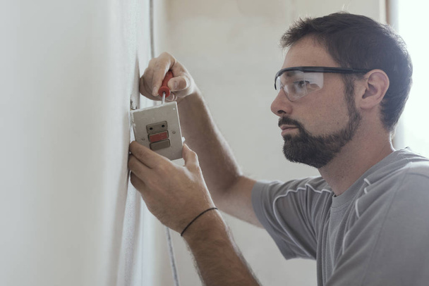 Electricista profesional instalando enchufes utilizando un destornillador: concepto de renovación y mantenimiento del hogar
 - Foto, imagen