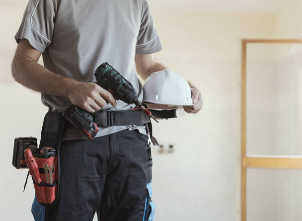 Construction worker posing with safety helmet and drill, home renovation and construction concept - Φωτογραφία, εικόνα