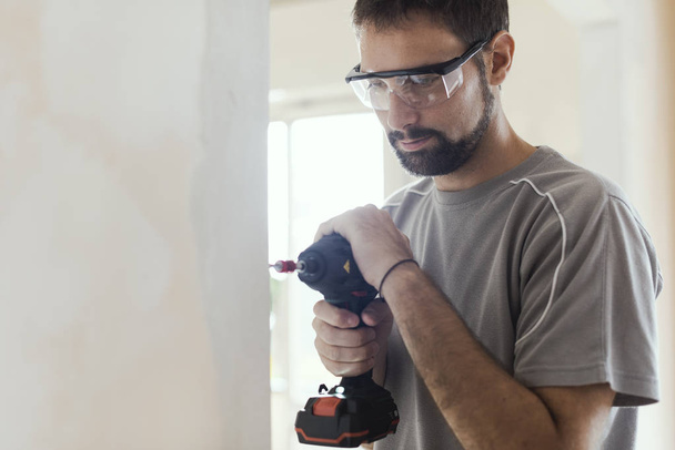 Professional repairman with protective goggles, he is using a drill and doing a home renovation - Zdjęcie, obraz