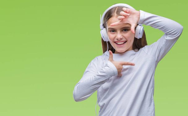 Young beautiful girl wearing headphones listening to music over isolated background smiling making frame with hands and fingers with happy face. Creativity and photography concept. - Photo, image