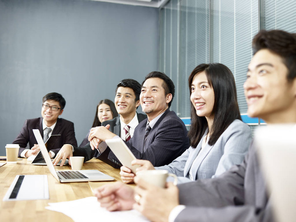ryhmä onnellisia hymyileviä aasialaisia liikemiehiä kuuntelemassa esitystä toimistohuoneessa
 - Valokuva, kuva
