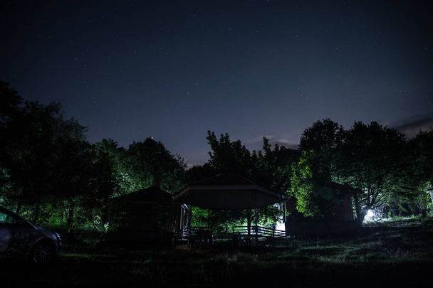 Гірський нічний пейзаж будівлі в лісі вночі з місяцем або старовинним заміським будинком вночі з хмарами і зірками. Літня ніч. Фото зроблено з тривалою експозицією
 - Фото, зображення