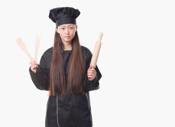 Jeune femme chinoise sur fond isolé portant uniforme de chef avec une expression confiante sur la pensée intelligente visage grave
 - Photo, image